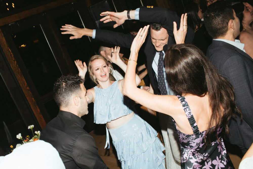 Group of guests dancing with arms raised at a party faces joyful in semi formal attire