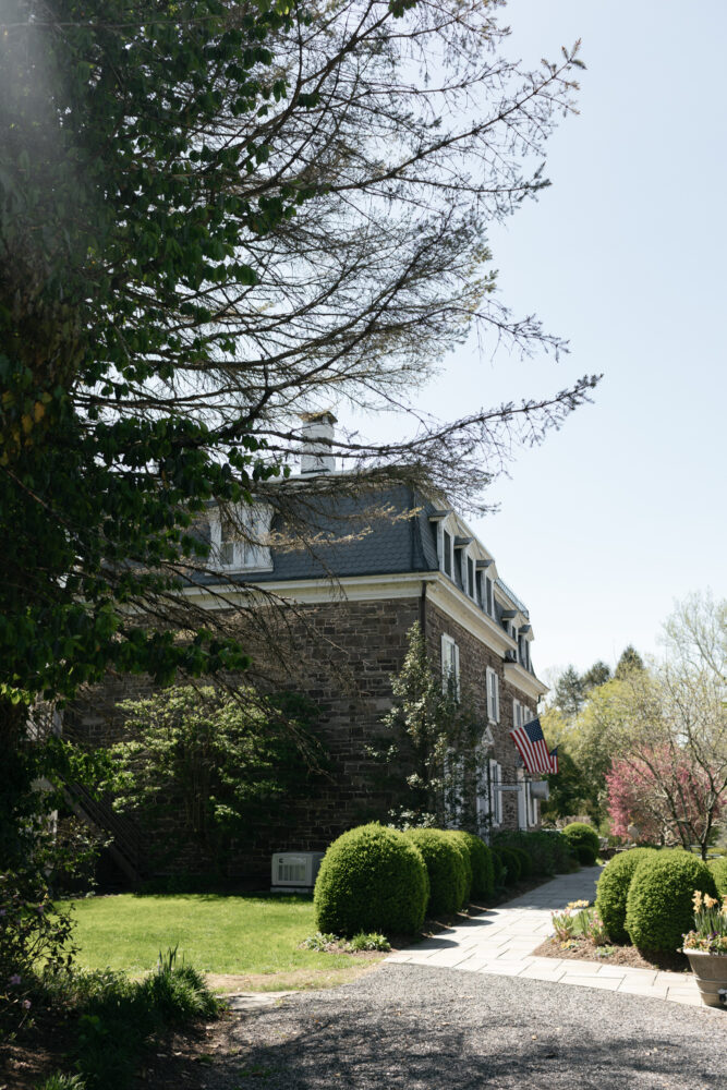 Stone townhouse with slate roof American flag along a paved garden path and manicured shrubs under a bright blue sky