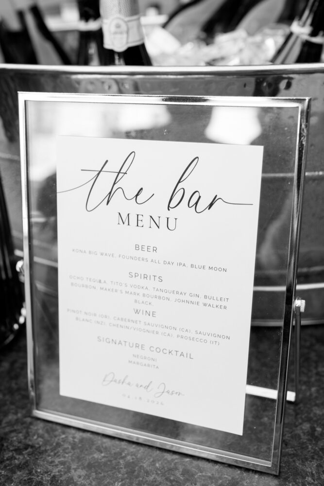 Framed bar menu card on a dark countertop with blurred bottles in the background the bar menu title reads the bar